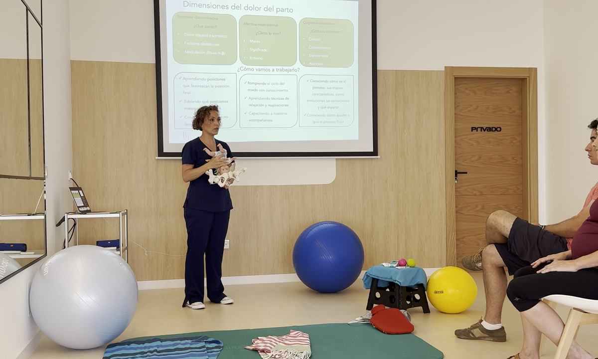 Bea Delgado, matrona en Alicante, explicando las dimensiones del dolor del parto con una pelvis anatómica durante una sesión del Método CALMA
